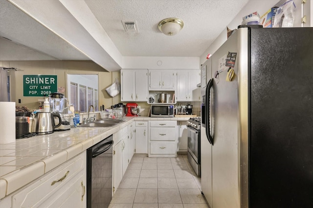 kitchen with appliances with stainless steel finishes, a sink, tile counters, and white cabinetry