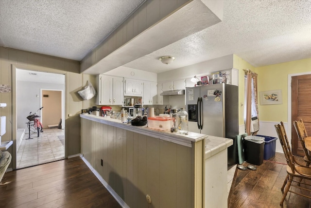 kitchen featuring dark wood-style flooring, stainless steel refrigerator with ice dispenser, tile counters, white cabinets, and a peninsula