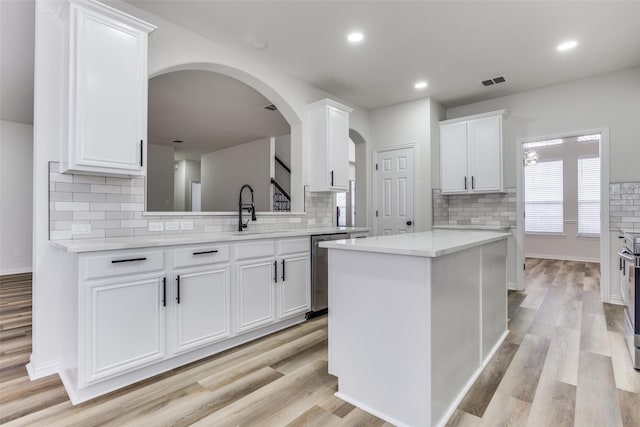 kitchen featuring visible vents, a center island, light countertops, white cabinetry, and a sink