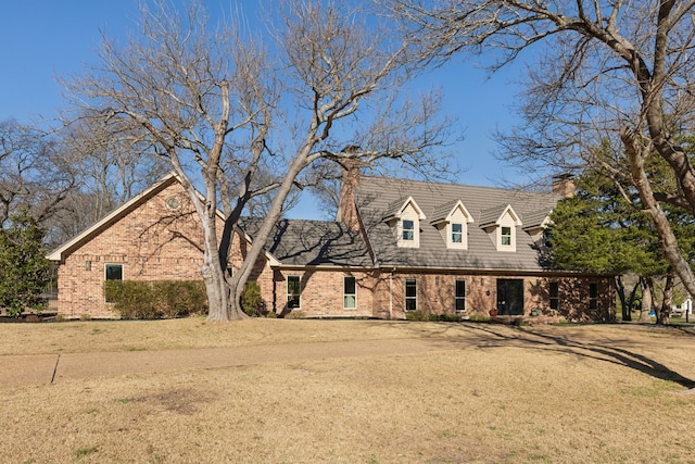 cape cod-style house featuring brick siding, a chimney, and a front lawn