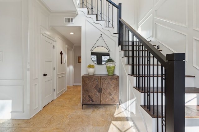 foyer entrance with visible vents, stairway, a decorative wall, and a towering ceiling