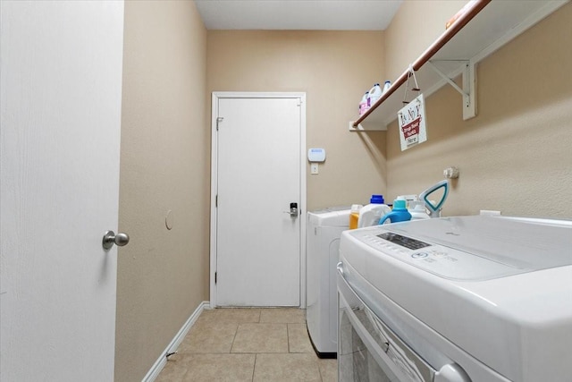 washroom featuring laundry area, baseboards, light tile patterned flooring, and washing machine and clothes dryer