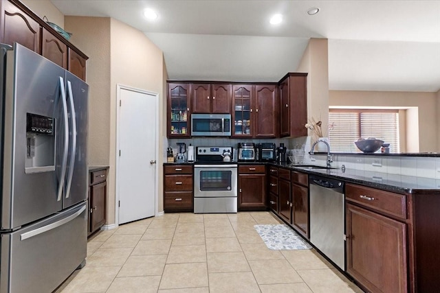 kitchen featuring glass insert cabinets, appliances with stainless steel finishes, dark stone countertops, a sink, and light tile patterned flooring