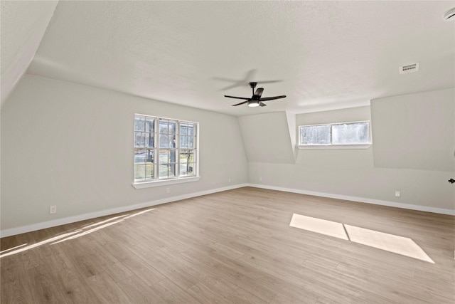 empty room with light wood-style flooring, a textured ceiling, visible vents, and baseboards