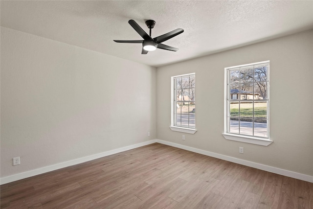 empty room featuring light wood-type flooring, ceiling fan, baseboards, and a textured ceiling