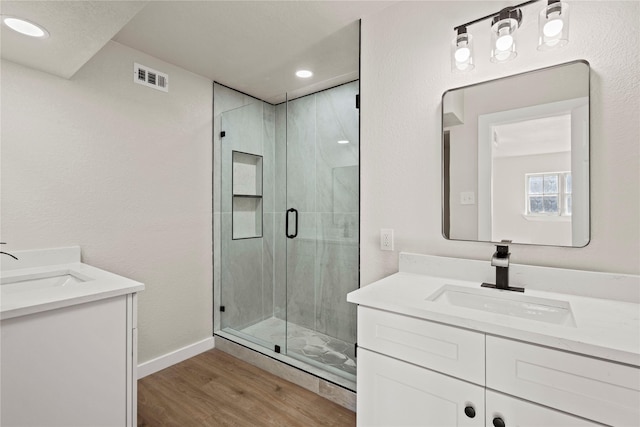 full bath featuring wood finished floors, two vanities, a sink, and a marble finish shower