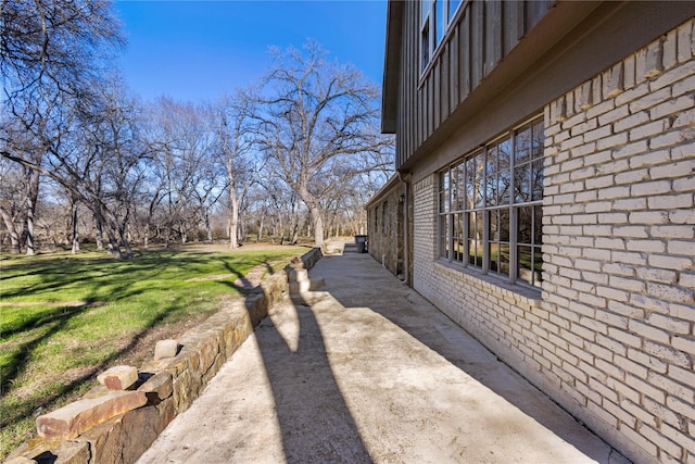 view of side of home featuring a yard, brick siding, and a patio area