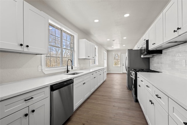 kitchen with stainless steel appliances, light countertops, white cabinets, a sink, and wood finished floors