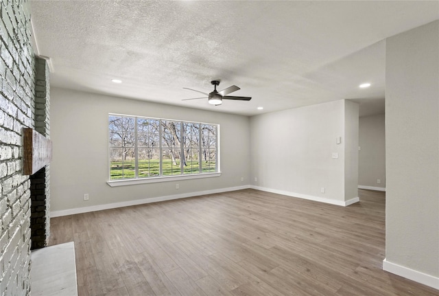 unfurnished living room with a textured ceiling, a brick fireplace, wood finished floors, and baseboards