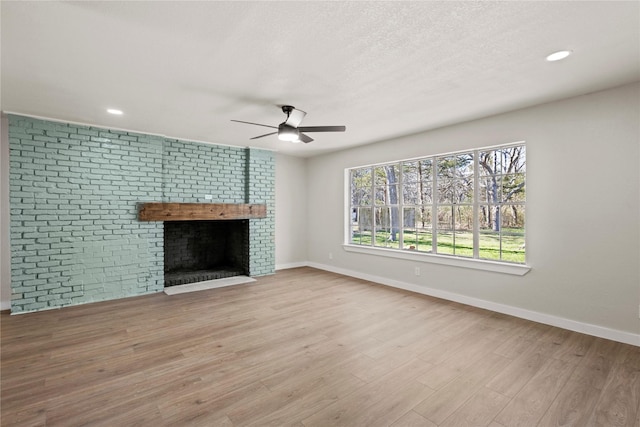 unfurnished living room featuring light wood-style flooring, a fireplace, baseboards, and a textured ceiling