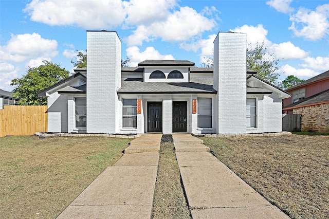 view of front facade with a chimney, fence, a front lawn, and brick siding