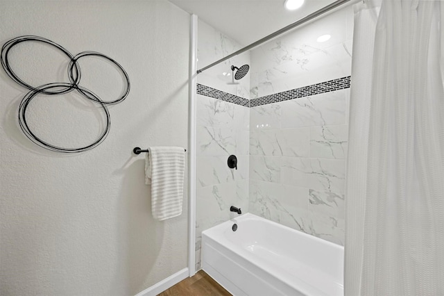 full bathroom featuring shower / bath combo, baseboards, wood finished floors, and a textured wall