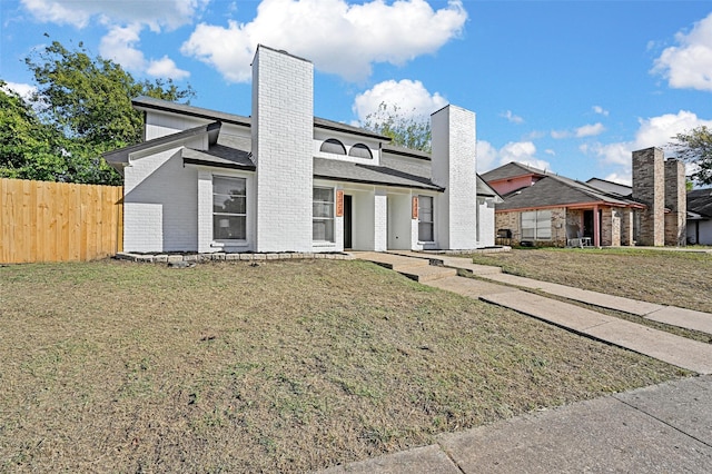 view of front of house featuring a chimney, fence, a front lawn, and brick siding