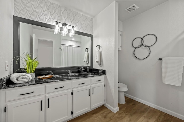 bathroom with visible vents, toilet, vanity, wood finished floors, and baseboards