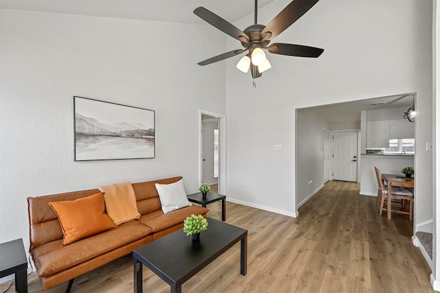 living room featuring a ceiling fan, wood finished floors, a towering ceiling, and baseboards