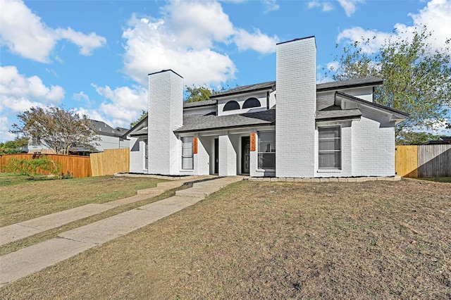 view of front of house with a front yard, fence, brick siding, and a chimney