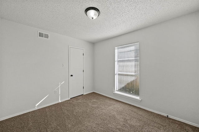 spare room featuring visible vents, baseboards, a textured ceiling, and dark carpet