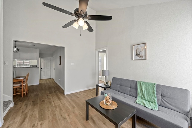 living room featuring a ceiling fan, baseboards, a towering ceiling, and light wood finished floors