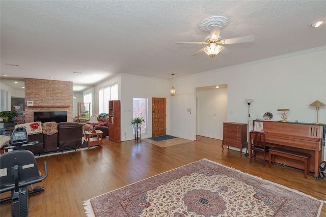 office area featuring a textured ceiling, ceiling fan, wood finished floors, a brick fireplace, and crown molding