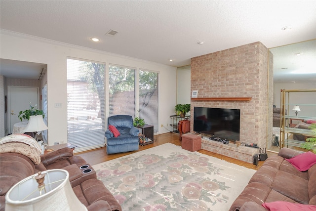 living room featuring crown molding, light wood finished floors, visible vents, a brick fireplace, and a textured ceiling