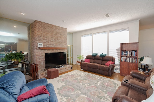 living room with a textured ceiling, light wood-style flooring, visible vents, ornamental molding, and a brick fireplace