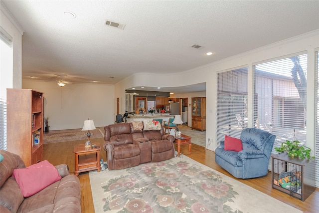 living room with ornamental molding, visible vents, a textured ceiling, and light wood finished floors