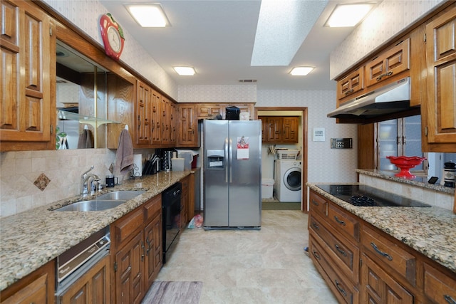 kitchen featuring wallpapered walls, washer / clothes dryer, brown cabinets, under cabinet range hood, and black appliances