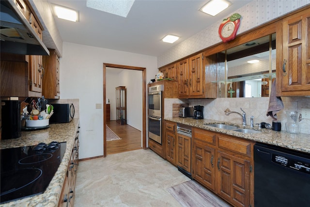 kitchen with light stone countertops, a sink, brown cabinets, decorative backsplash, and black appliances