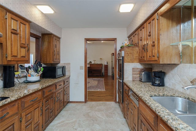 kitchen with black microwave, brown cabinetry, a sink, and light stone countertops