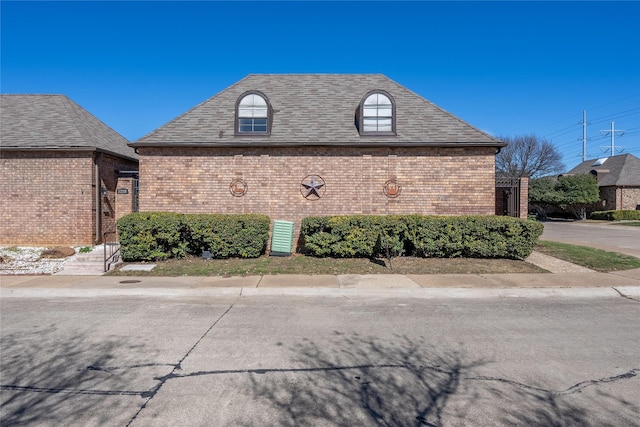 view of side of home featuring brick siding and a shingled roof