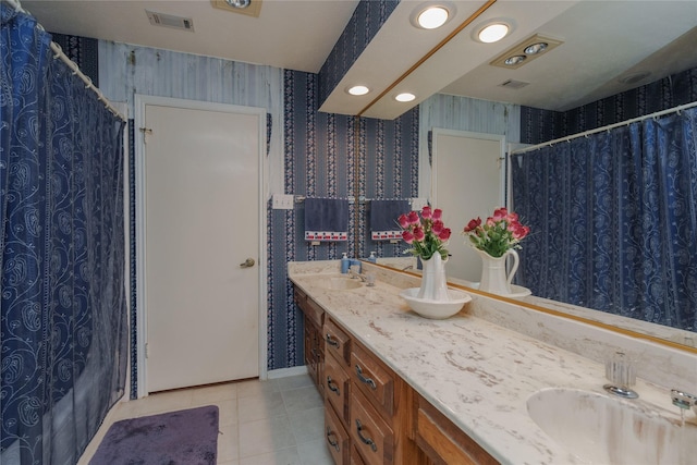 bathroom with double vanity, visible vents, wallpapered walls, a sink, and tile patterned floors