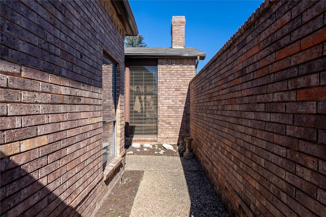 view of property exterior with a shingled roof, a chimney, and brick siding