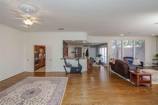 living room featuring light wood-style flooring, visible vents, a textured ceiling, and ornamental molding