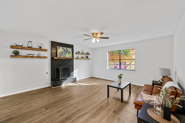 living room featuring a brick fireplace, wood finished floors, a ceiling fan, and baseboards