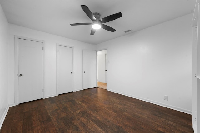 unfurnished bedroom featuring baseboards, visible vents, ceiling fan, dark wood-style flooring, and two closets