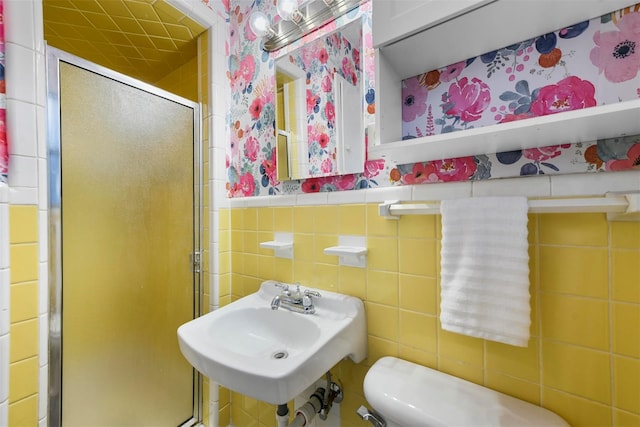 bathroom featuring tile walls, a stall shower, wainscoting, a sink, and wallpapered walls