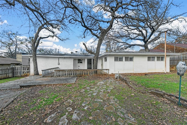 rear view of house featuring brick siding, fence, and a wooden deck