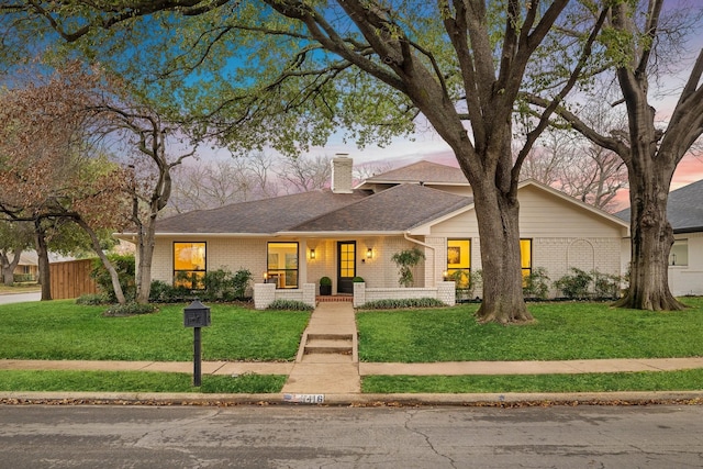 mid-century inspired home featuring a shingled roof, a chimney, fence, a front lawn, and brick siding