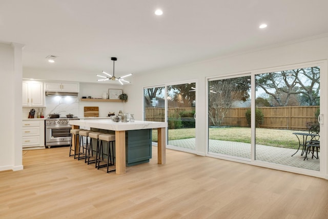 kitchen with open shelves, light countertops, white cabinetry, high end range, and a kitchen bar