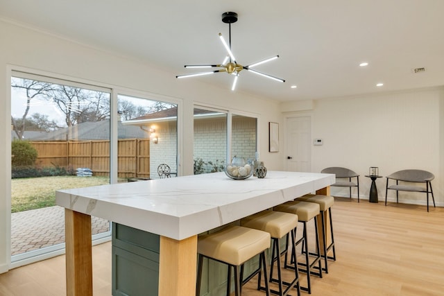 kitchen featuring baseboards, light stone counters, crown molding, light wood-style floors, and recessed lighting