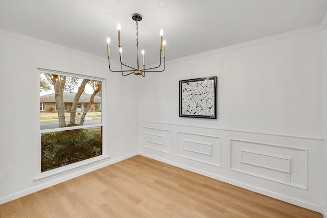 unfurnished dining area with ornamental molding, a chandelier, wood finished floors, and a decorative wall