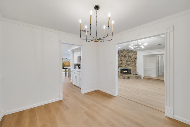 unfurnished dining area with crown molding, light wood finished floors, a fireplace, and a notable chandelier