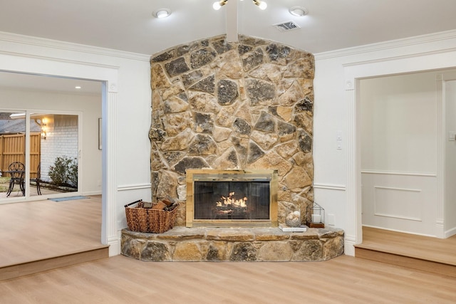 living area with ornamental molding, a stone fireplace, wood finished floors, and visible vents