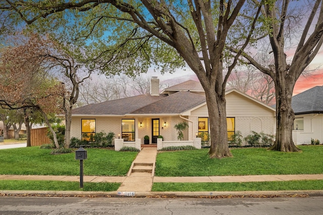 mid-century modern home with brick siding, a chimney, a front yard, and a shingled roof