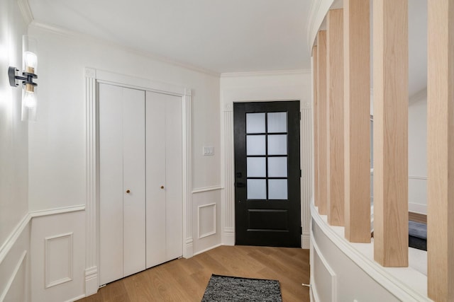 entryway featuring light wood-style floors, ornamental molding, and a decorative wall