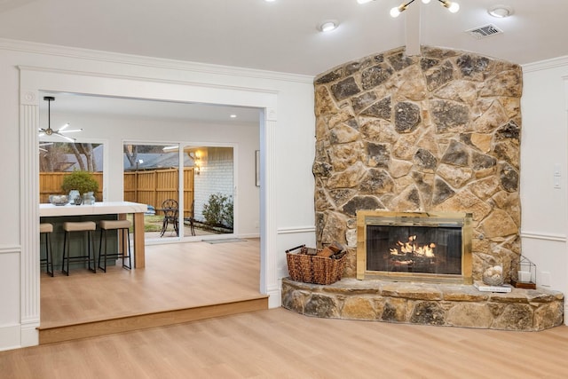 living area featuring visible vents, crown molding, a stone fireplace, and wood finished floors