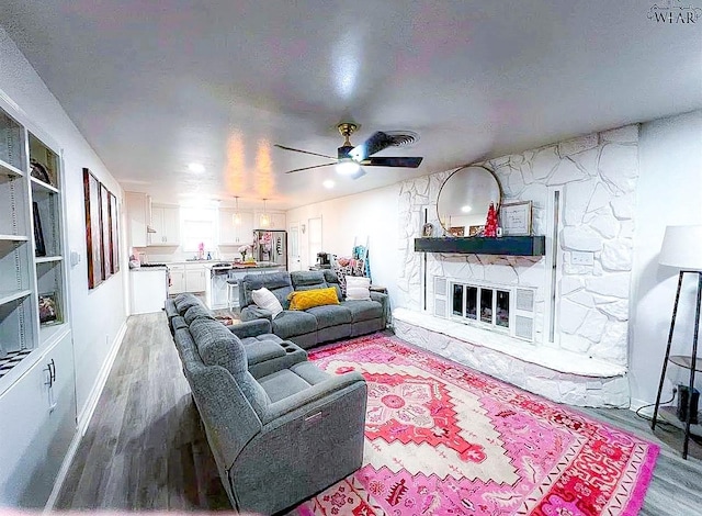 living room with a stone fireplace, a textured ceiling, a ceiling fan, and wood finished floors