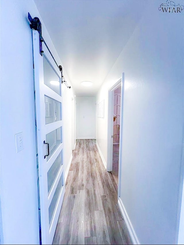 hall featuring a barn door, wood finished floors, and baseboards