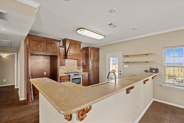 kitchen featuring stainless steel range with gas cooktop, light countertops, premium range hood, and a peninsula