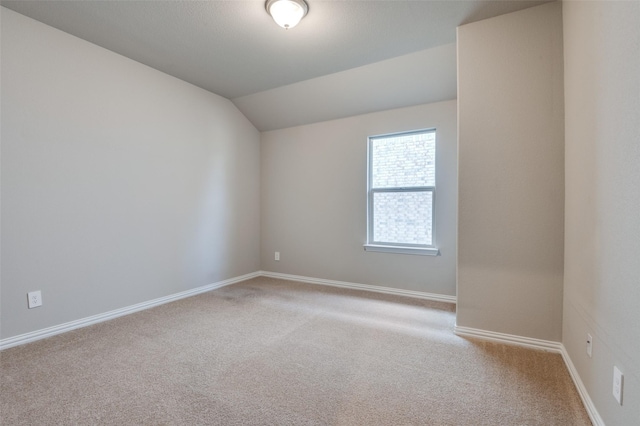 empty room featuring light colored carpet, vaulted ceiling, and baseboards